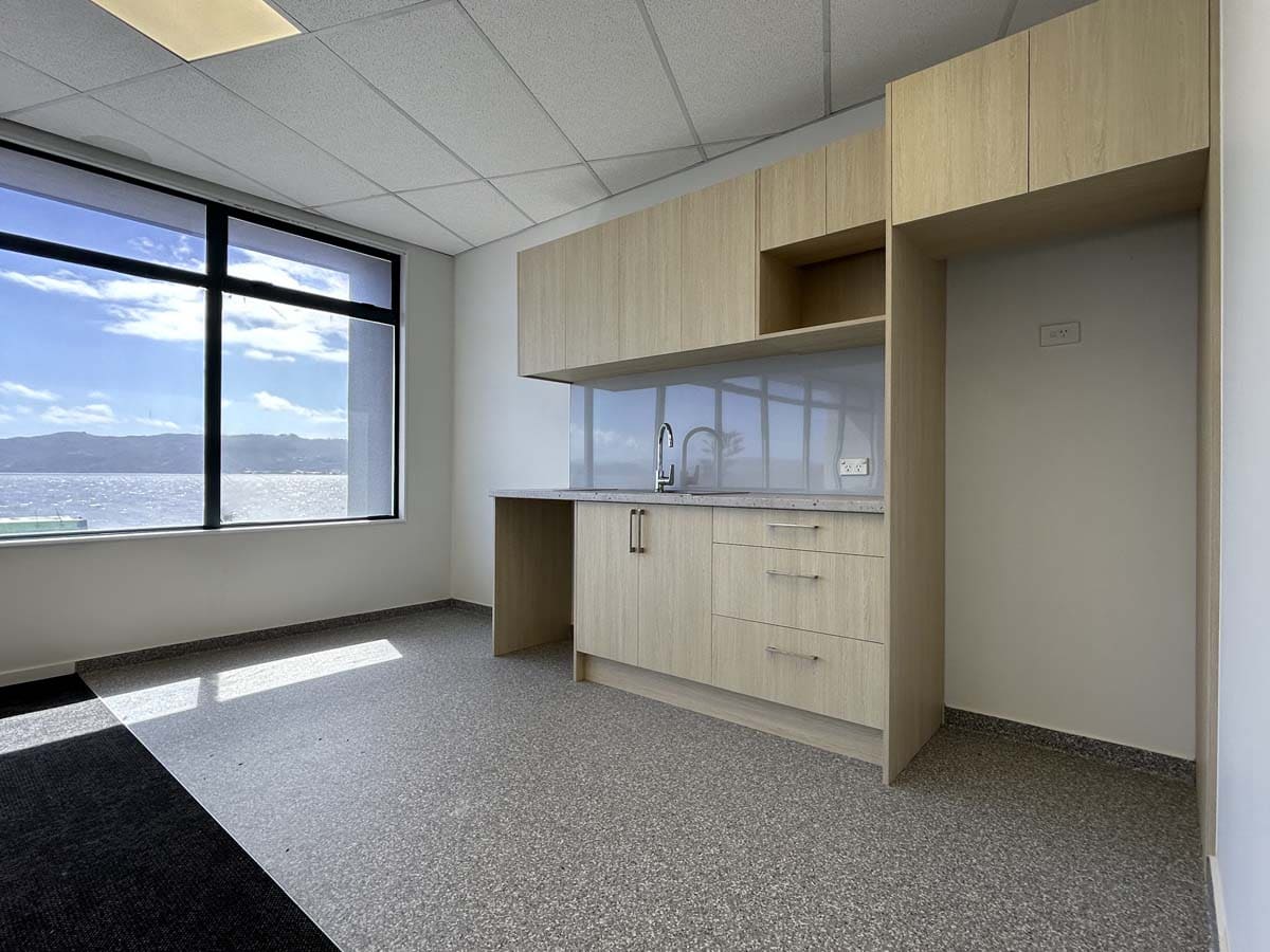Modern office kitchen with large window and light wood cabinetry.