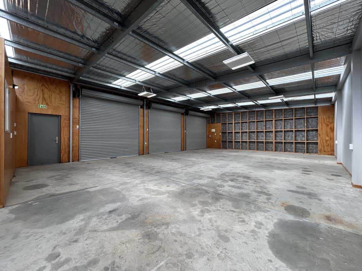 Indoor industrial warehouse space with high ceilings and metal roller doors.