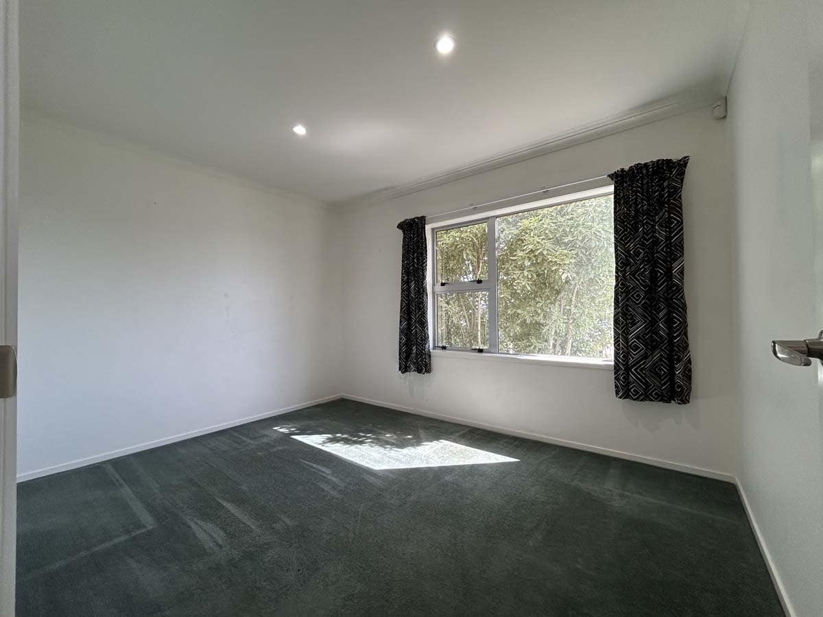 Interior of a bright, empty room with a large window and black curtains.