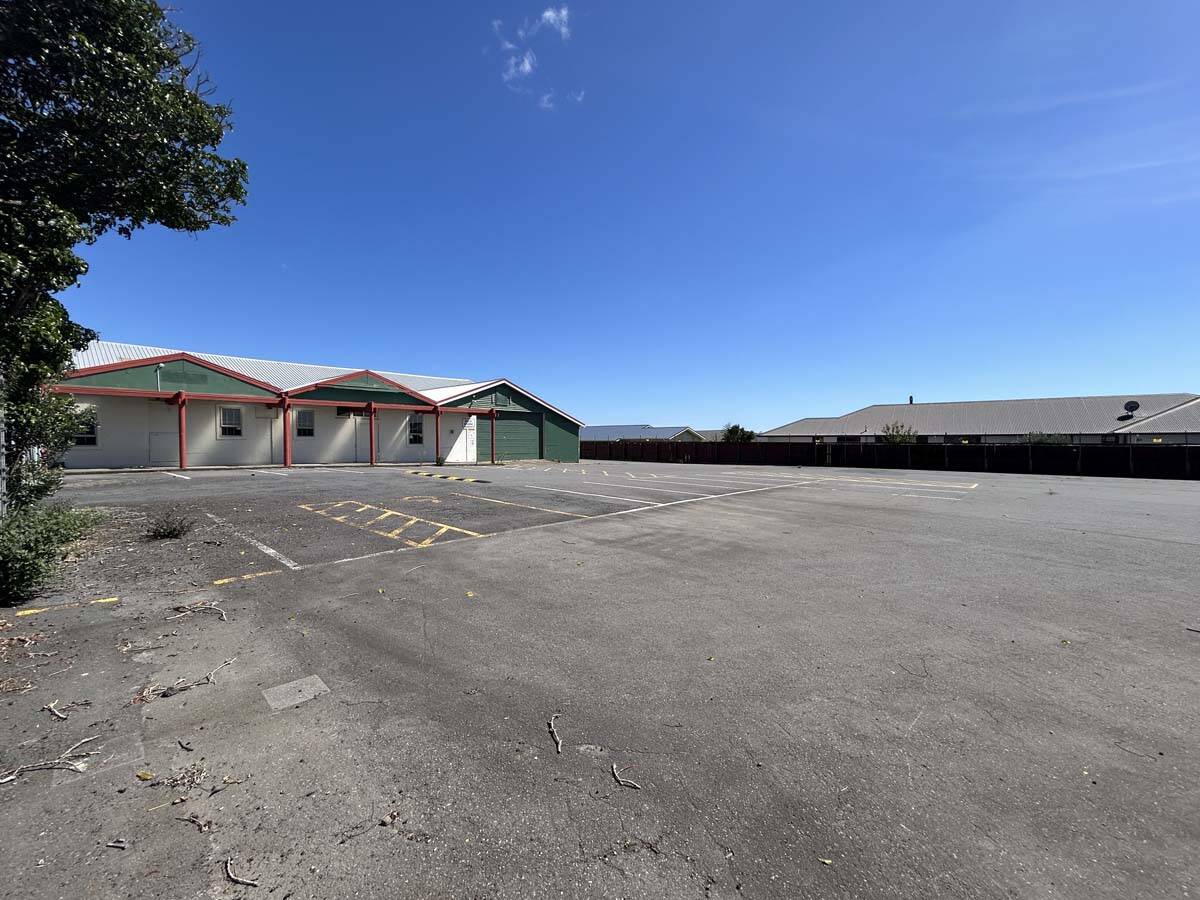 Empty parking lot with commercial buildings under clear blue sky.