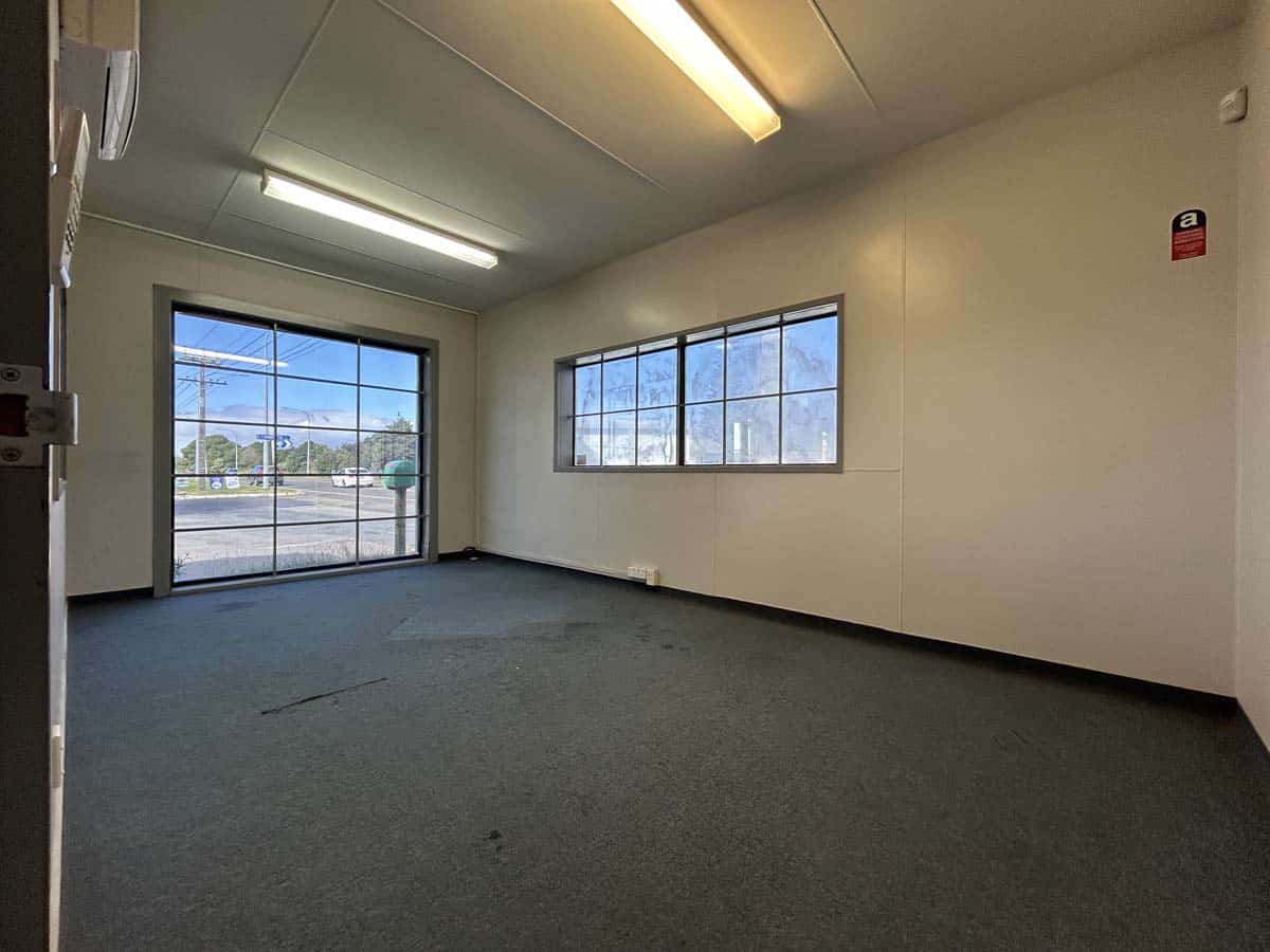 Bright empty office room with large windows and fluorescent lighting.