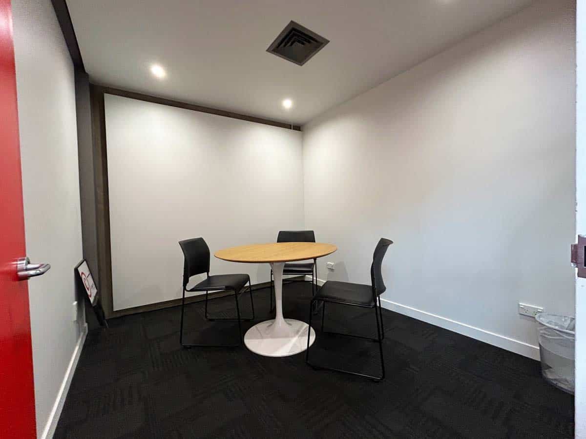 Interior view of a modern meeting room with a round table and three chairs.