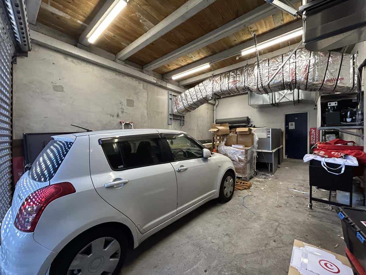 Garage interior with a silver car parked, storage shelves, and industrial ducting.