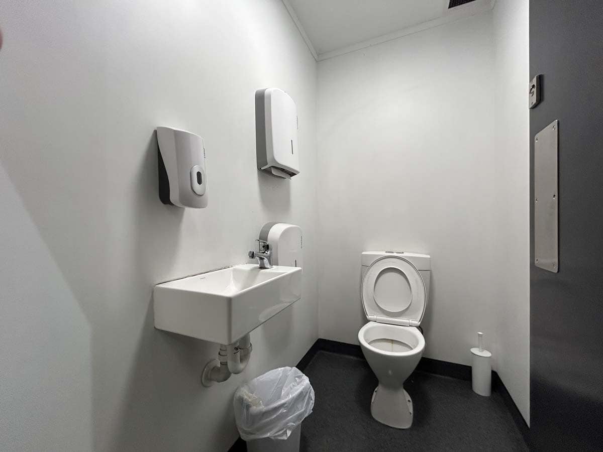Clean commercial restroom with sink, toilet, and hygiene supplies.