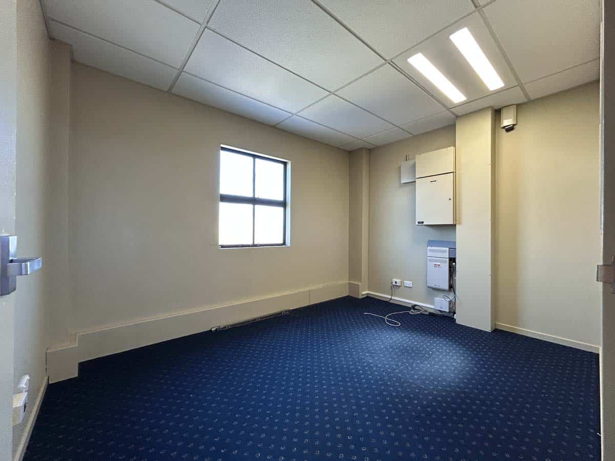 Empty office space with window, ceiling lights, and electrical outlets.