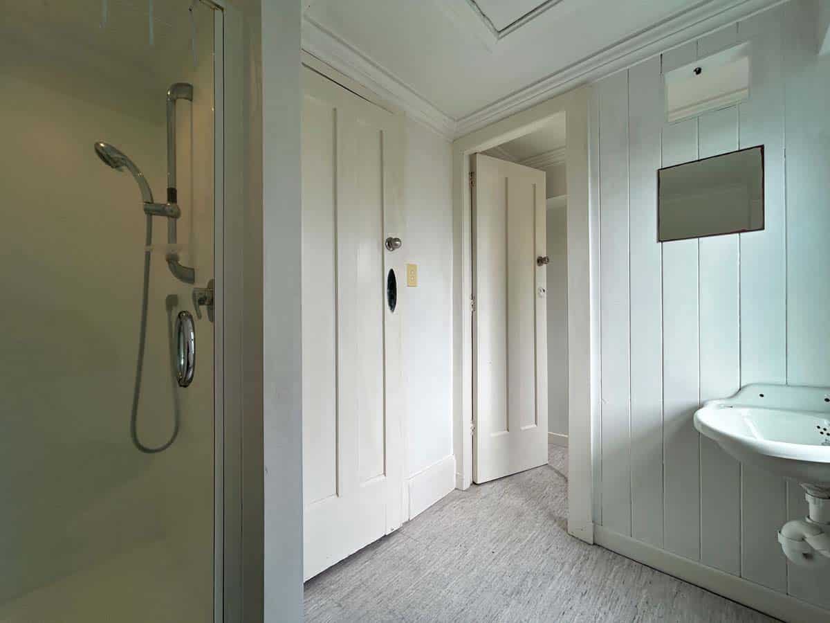 Interior view of a bathroom at 74 Powderham Street, featuring a shower, white walls, and a small sin.