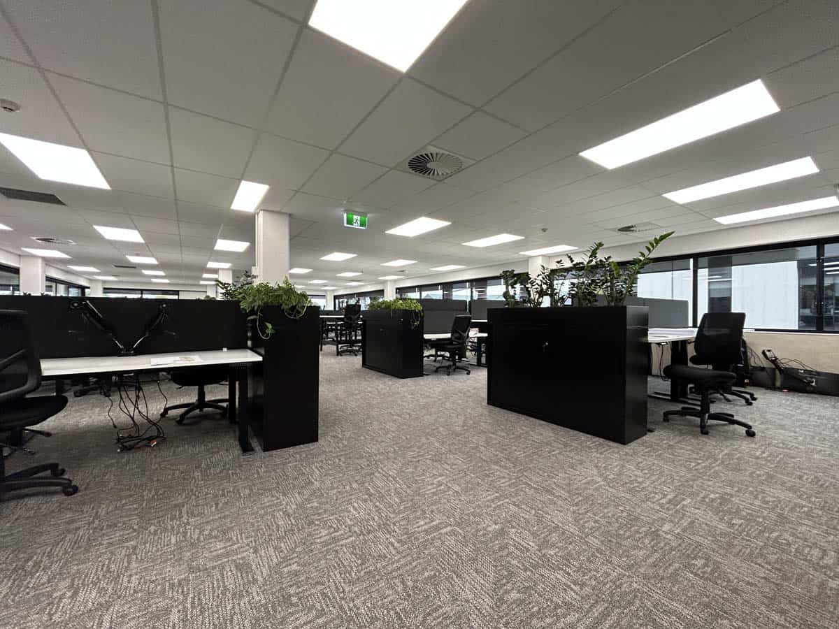 Open-plan office with desks, chairs, and plants in a modern workspace.