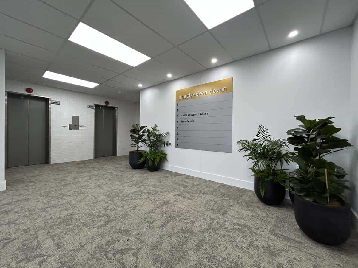 Modern office lobby featuring potted plants and a directory board.