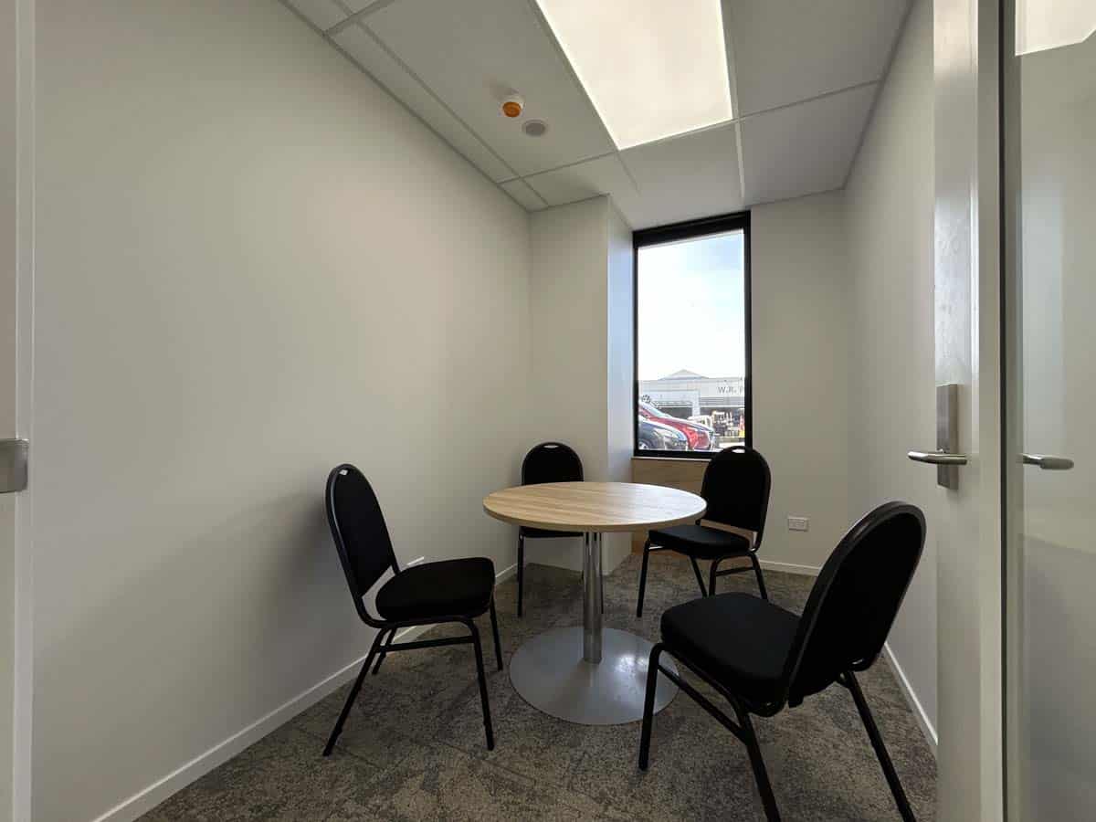Modern meeting room with round table and four black chairs, bright natural light.