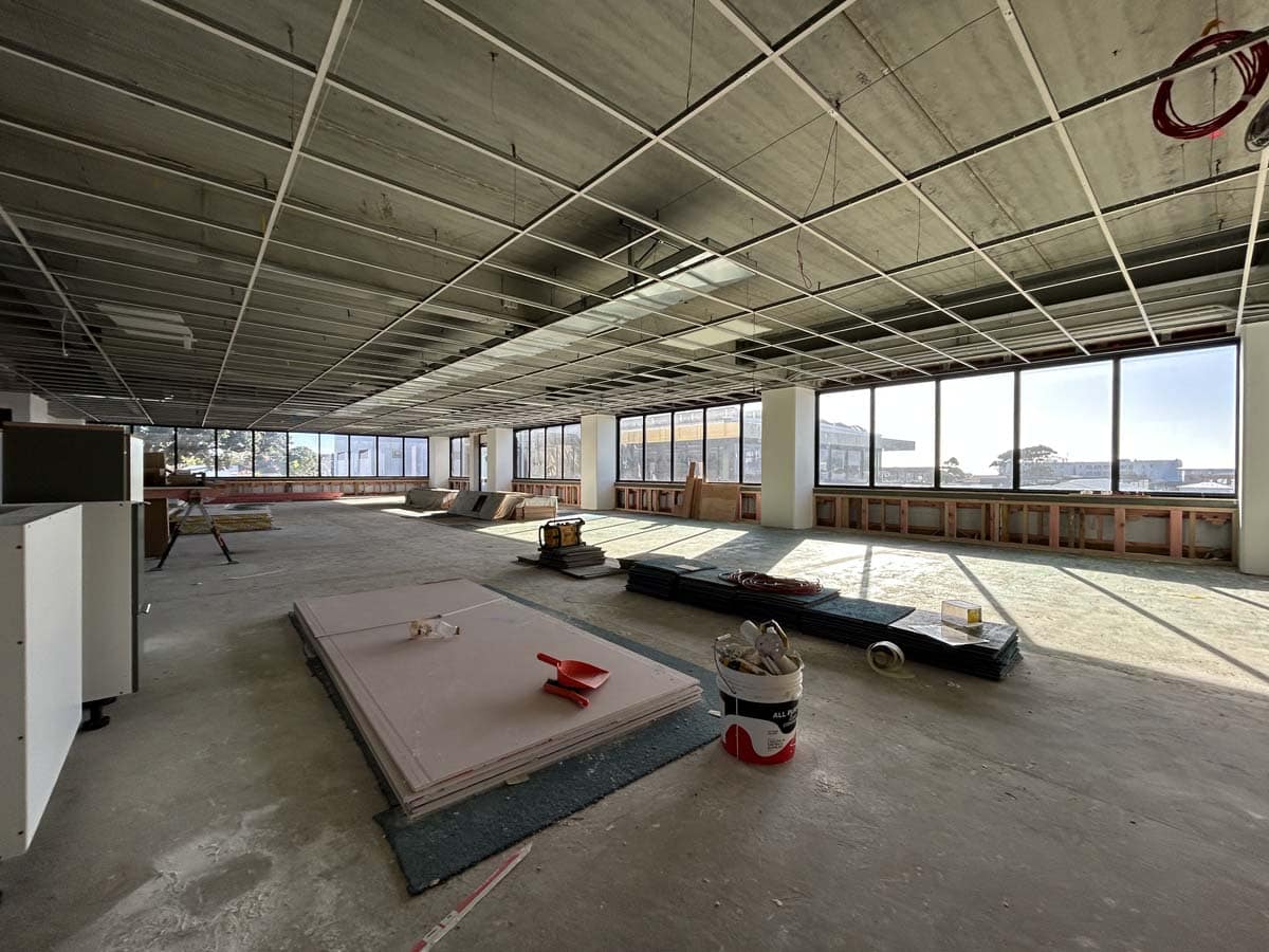 Interior view of a building under construction with large windows and construction materials.