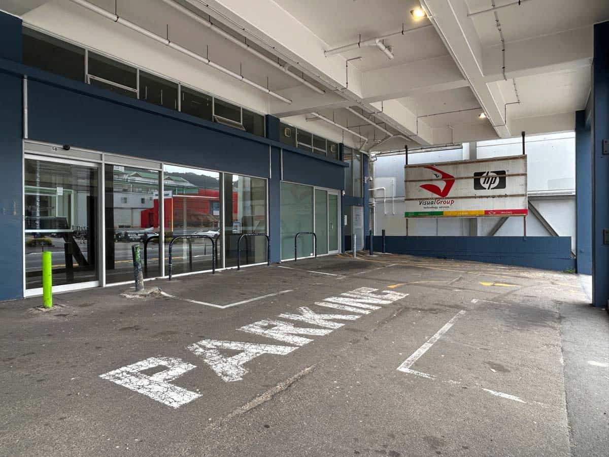Parking space with "PARKING" sign in front of a modern commercial building.