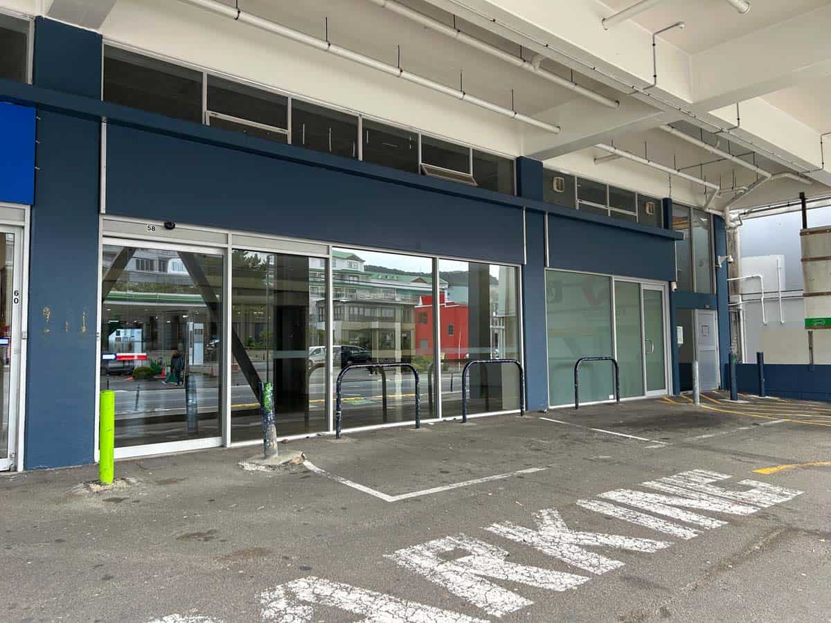 Modern commercial building entrance with glass doors and parking area.