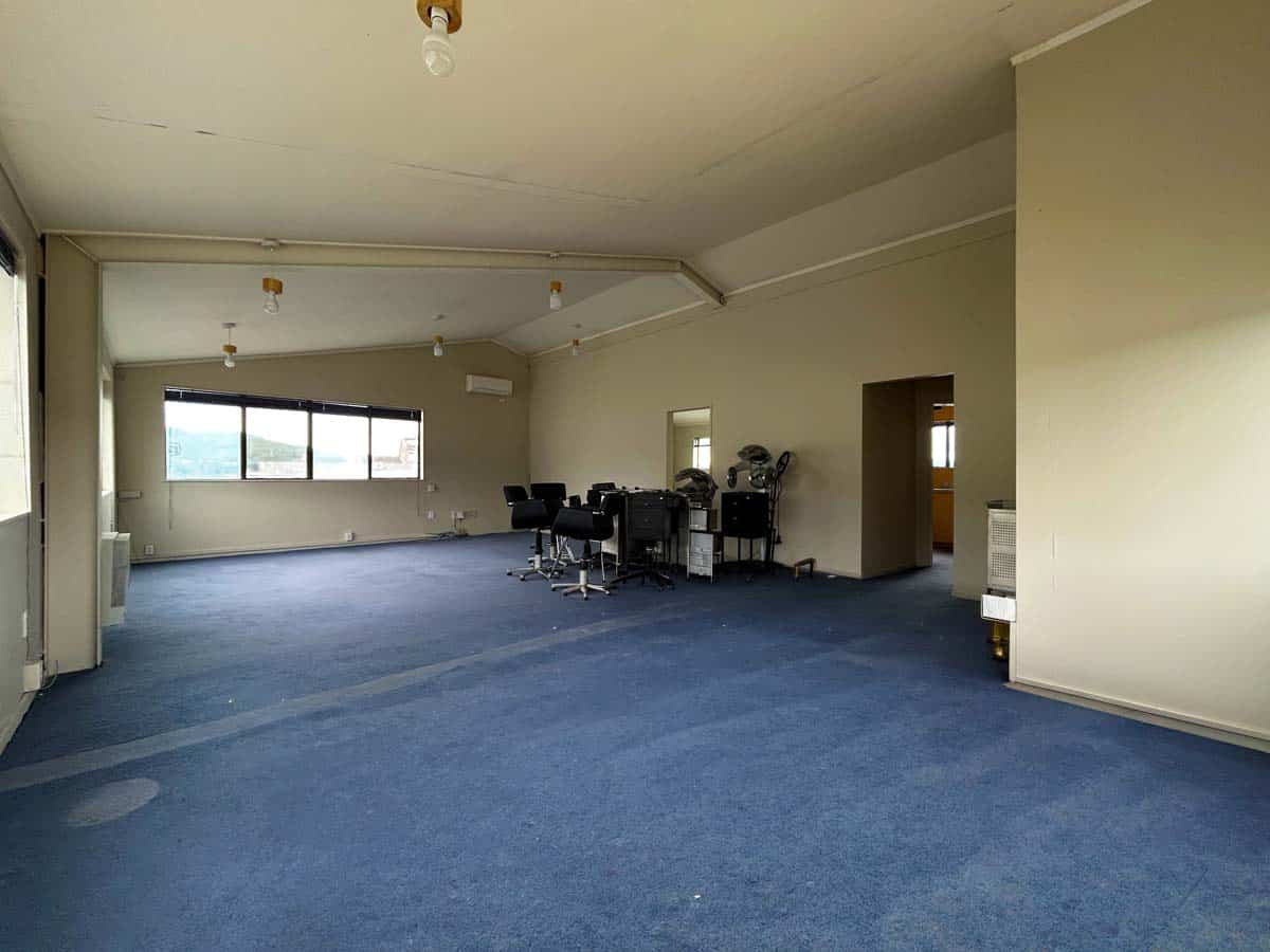 Office space with desks, large windows, and blue carpet flooring.