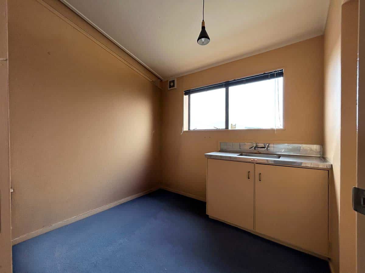 Small kitchen with beige walls, blue carpet, window, and sink cabinet.