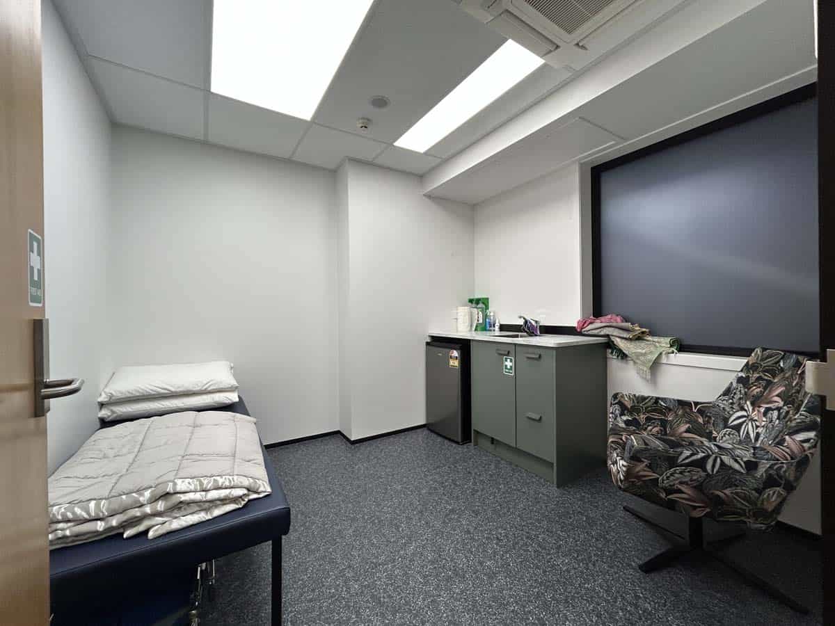 Empty medical consultation room with bed, cabinets, and large screen.
