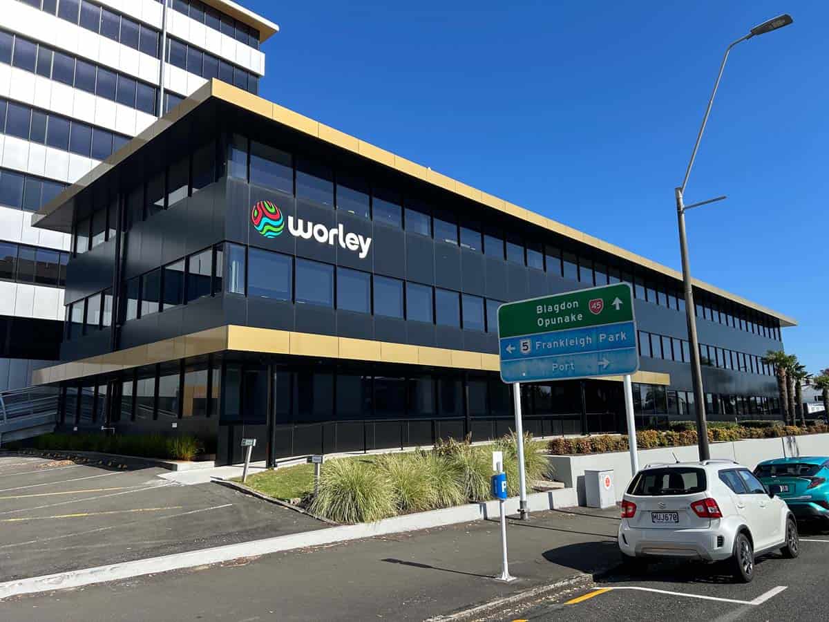 Modern office building with Worley logo, parking lot, and directional signs in Auckland.