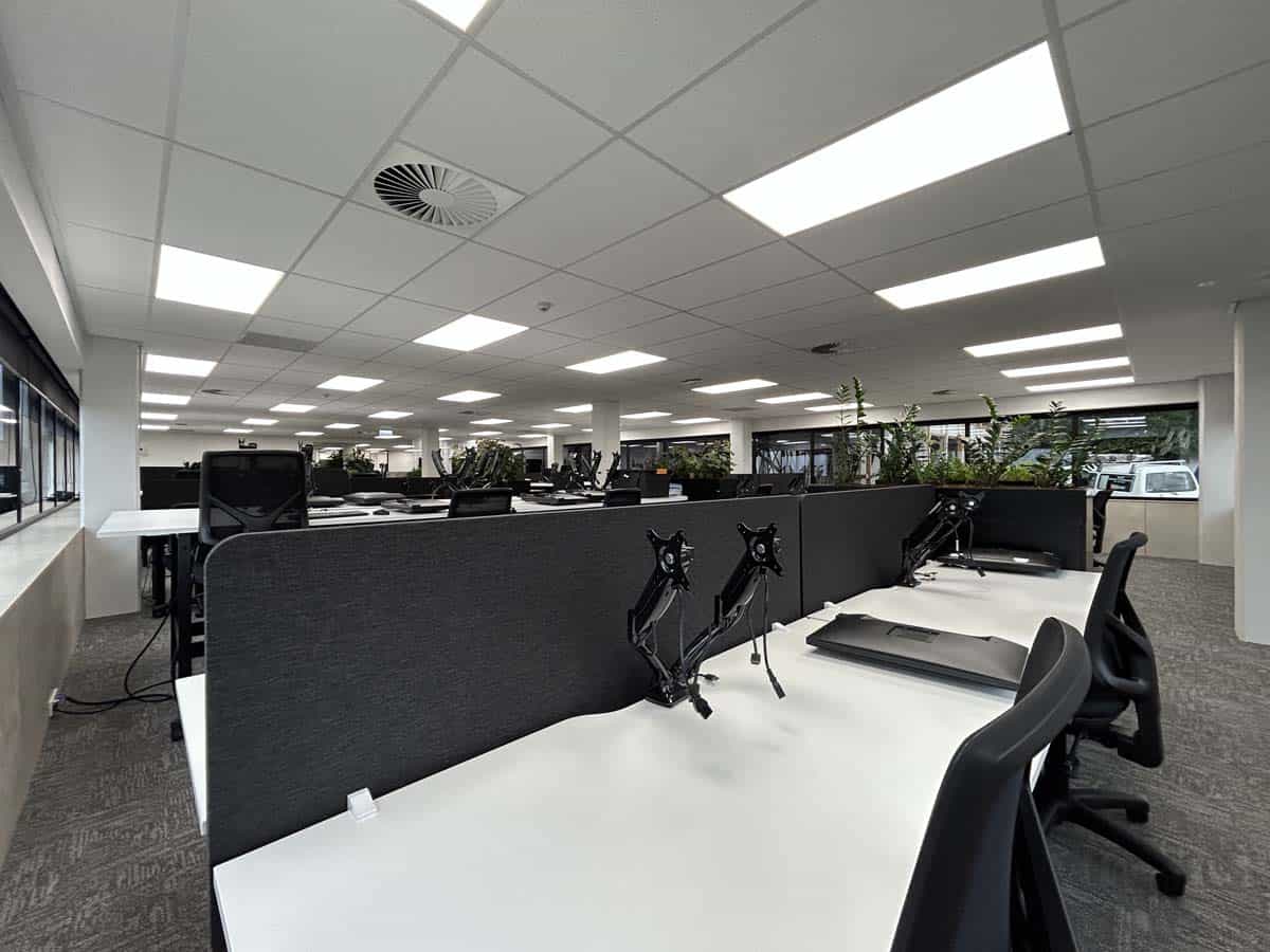 Modern office interior with workstations, chairs, and ceiling lighting.