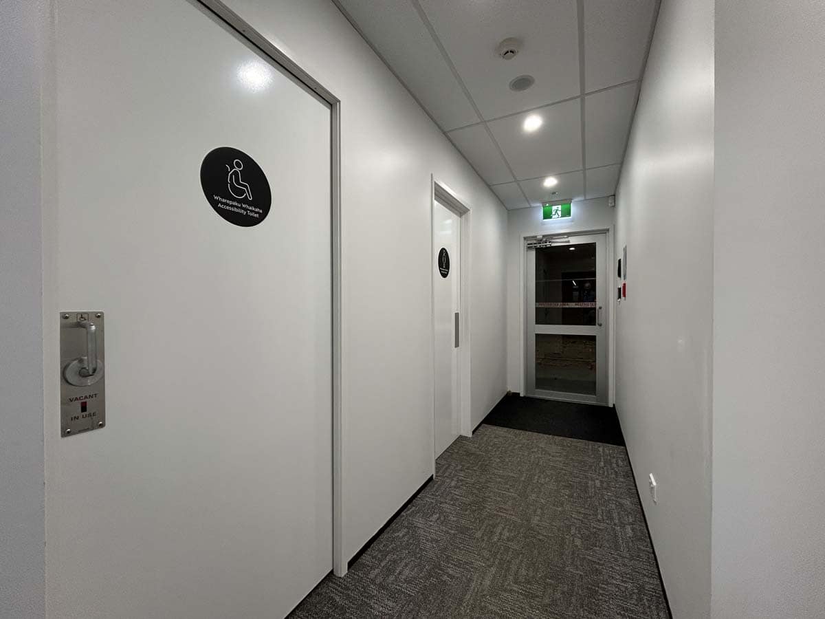 Modern office corridor with accessible restroom door and emergency exit.