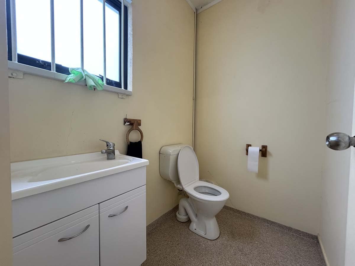 Simple bathroom with a white toilet, sink, and a small window in a neutral setting.