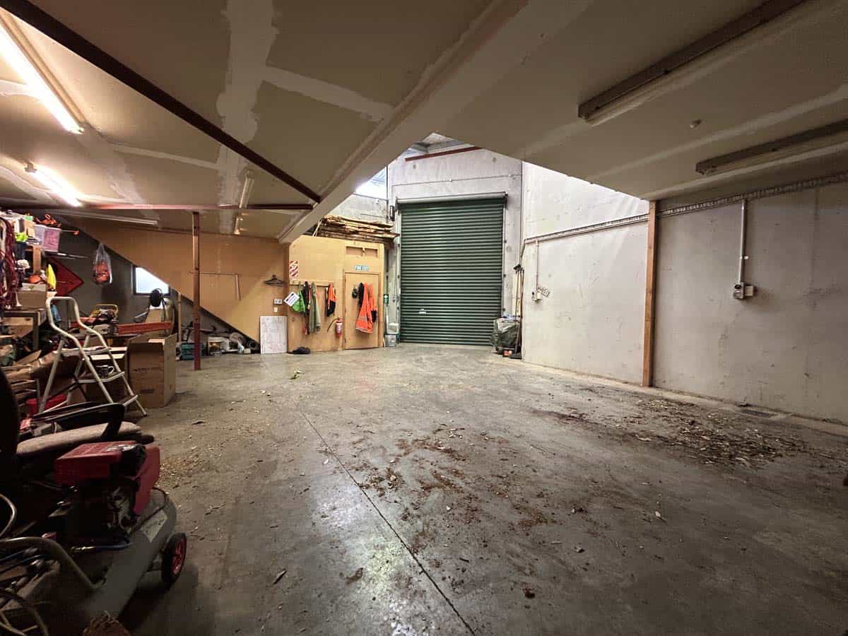 Empty storage unit with a green roll-up door and concrete floor.