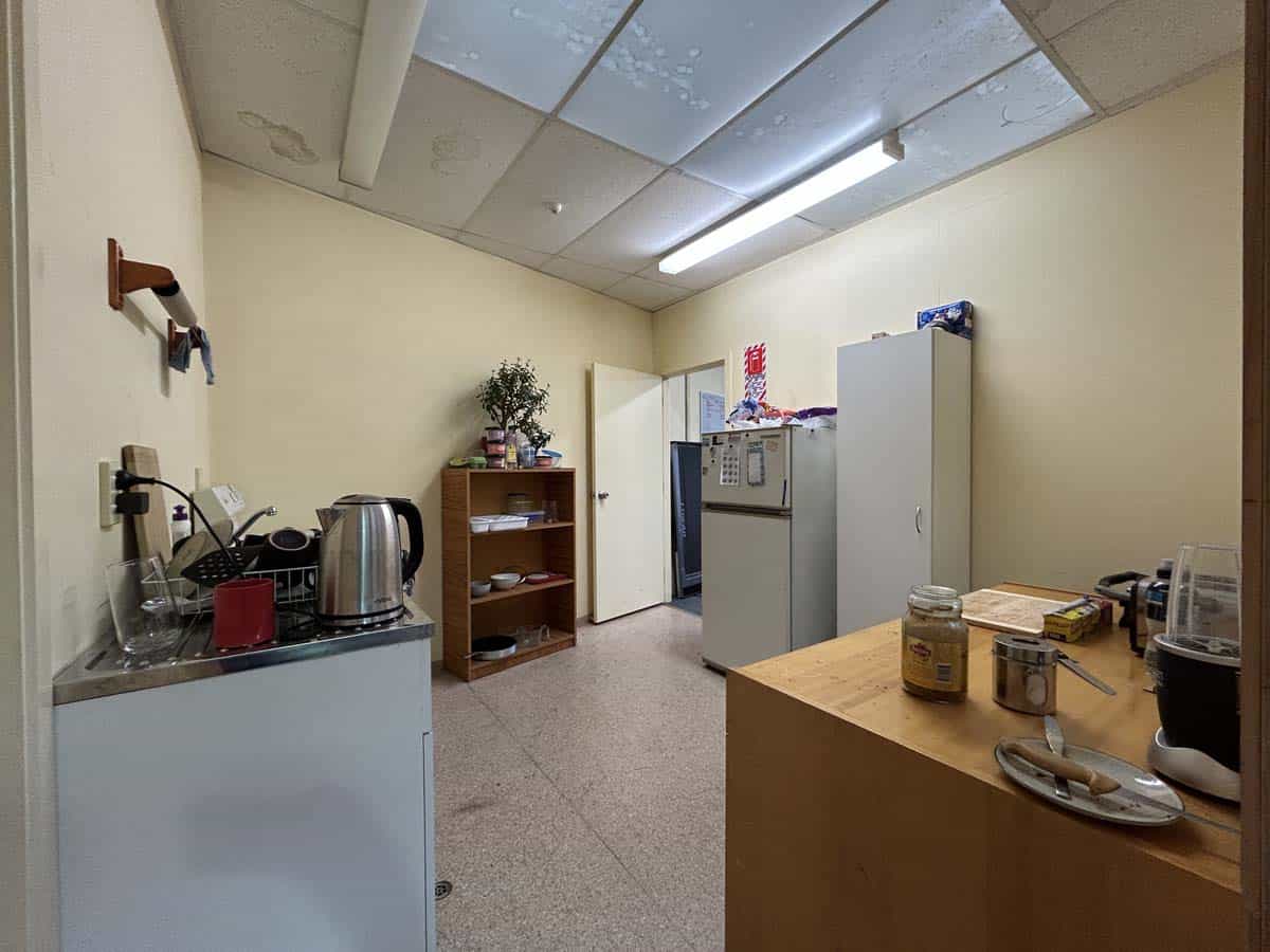 Interior view of a small office kitchen with appliances, shelves, and supplies.