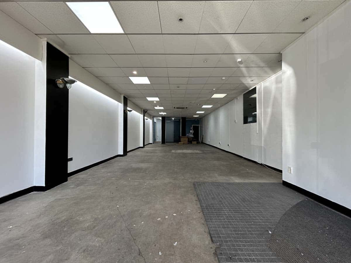 Interior view of a sleek, empty office hallway with white walls and ceiling lights.