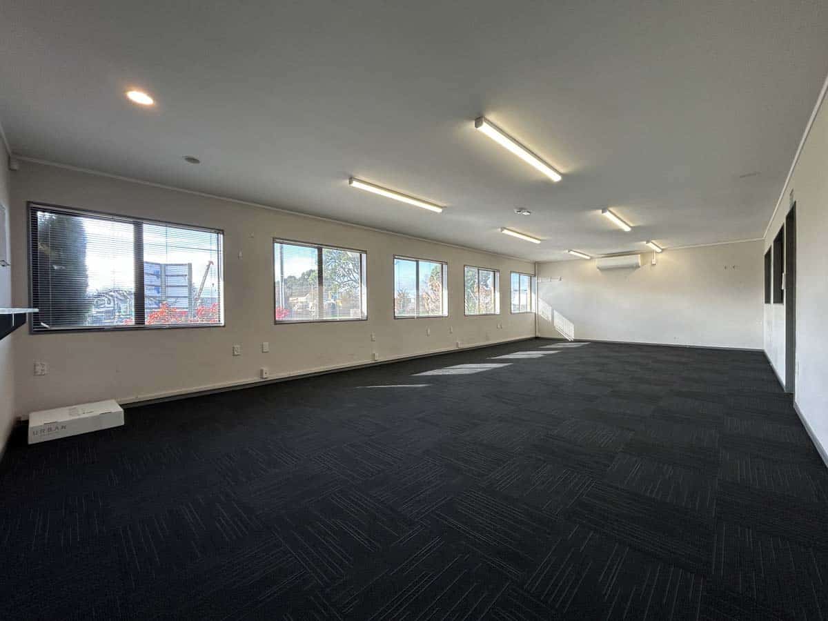 Spacious empty office with large windows, modern lighting, and dark carpet flooring.