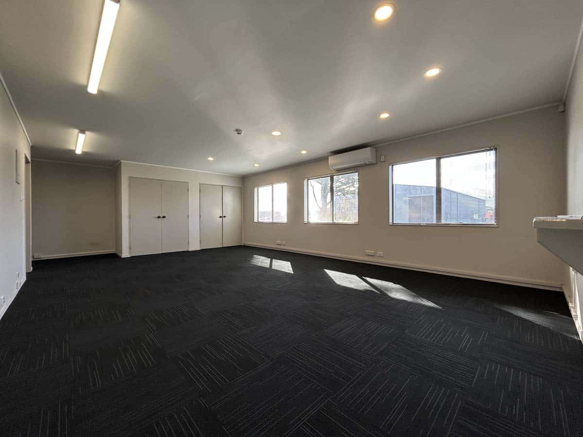 Spacious modern office room with large windows and ceiling lighting.