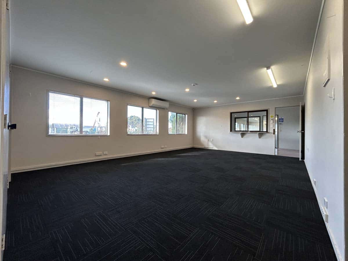 Spacious office interior featuring large windows, black carpet, and bright lighting.