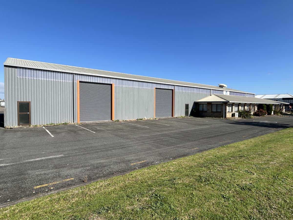 Modern industrial warehouse with large roller doors and parking area.