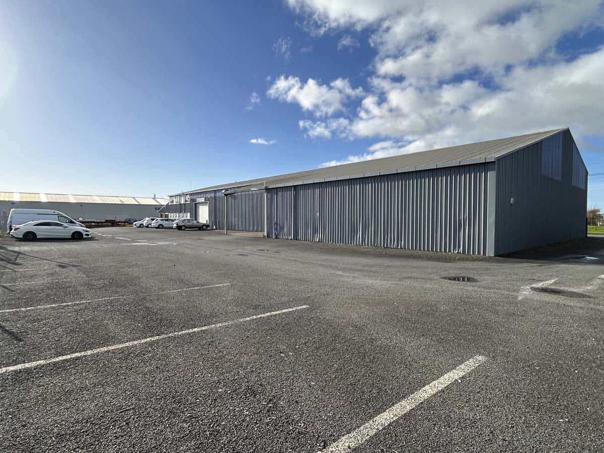Large industrial warehouse with metal siding and parking lot under a blue sky.