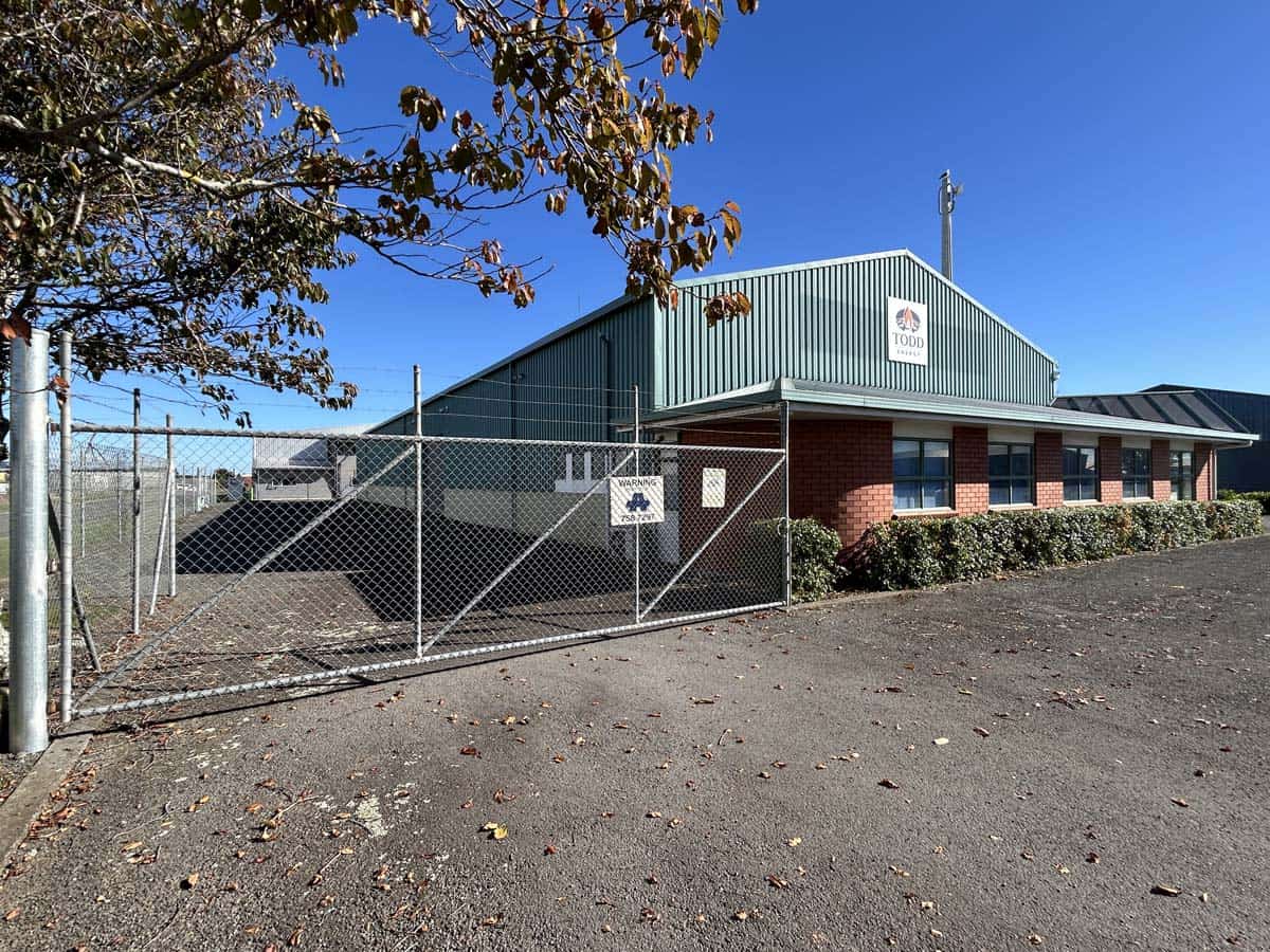 Warehouse building with chain-link fence and blue sky.
