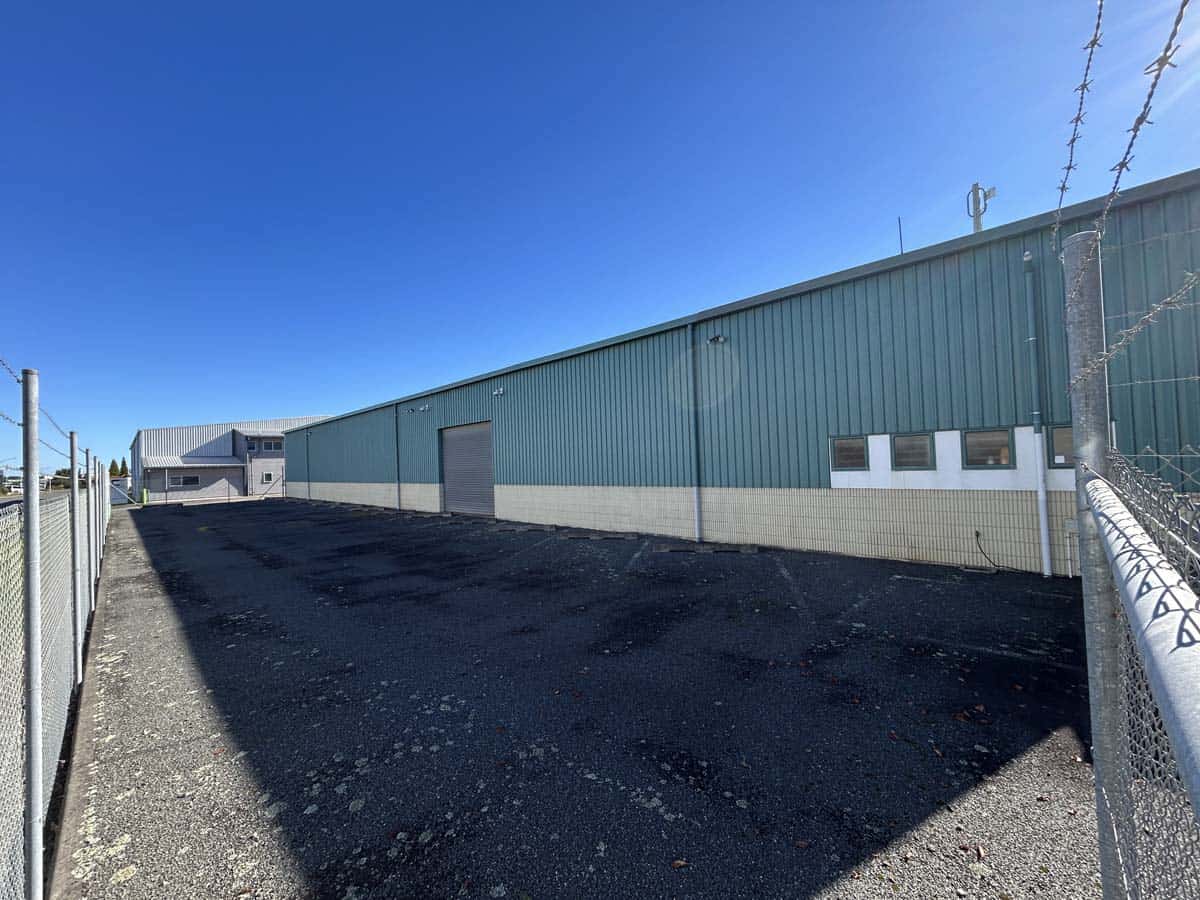 Large green industrial warehouse with a paved driveway and clear blue sky.