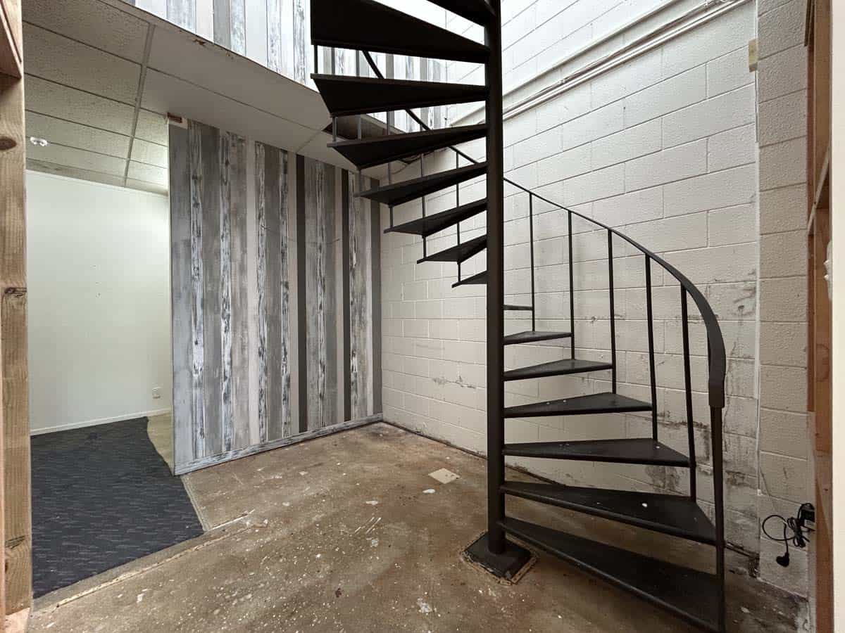 Modern black spiral staircase in minimalist interior with concrete floor and white brick wall.