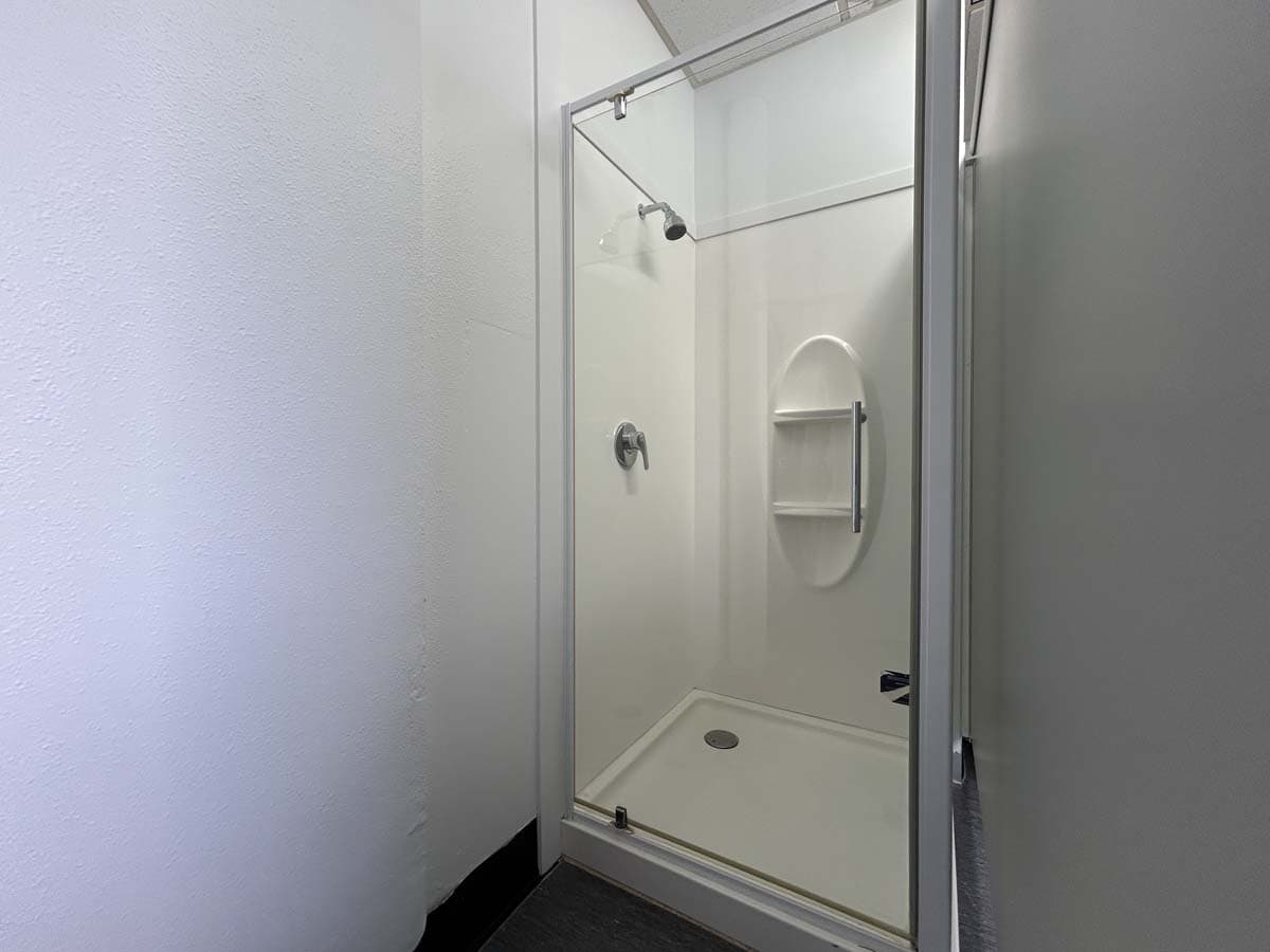 Modern white shower cabin with glass door and built-in shelf.