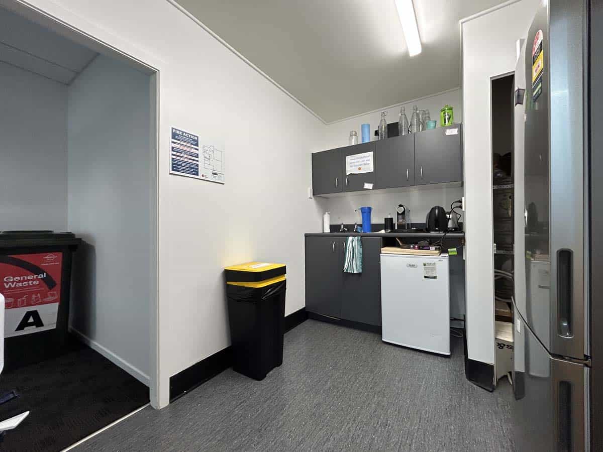 Office kitchenette with fridge, cabinets, and cleaning supplies.