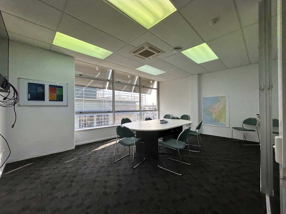 Modern office meeting room with large windows, conference table, and chairs.