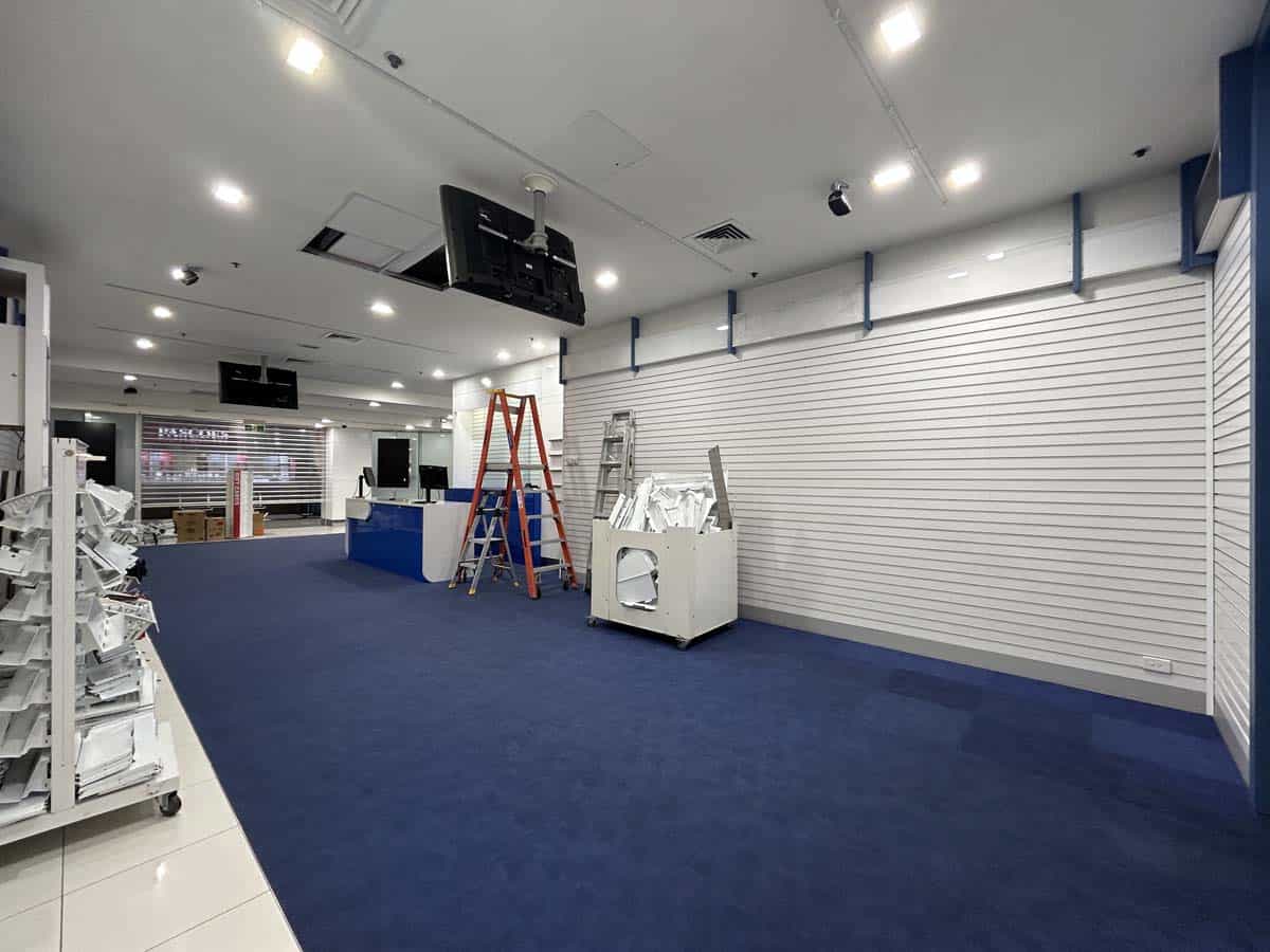 Empty retail store with blue carpet, display shelves, and ceiling monitors.
