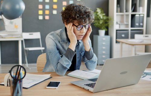 Woman looking overwhelmed at her laptop, illustrating ADHD task paralysis and difficulty starting tasks.