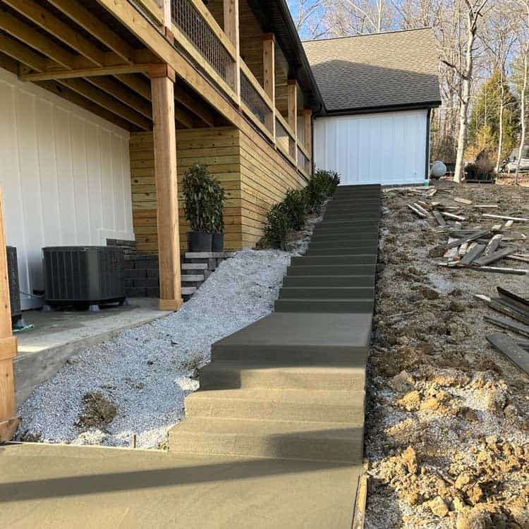 Concrete staircase leading to a residential outdoor area with landscaping and construction materials.