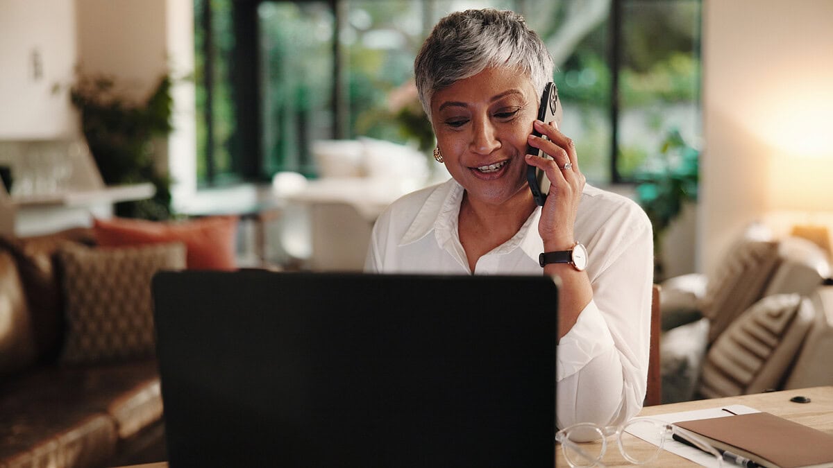 women sat at a laptop while on her mobile phone