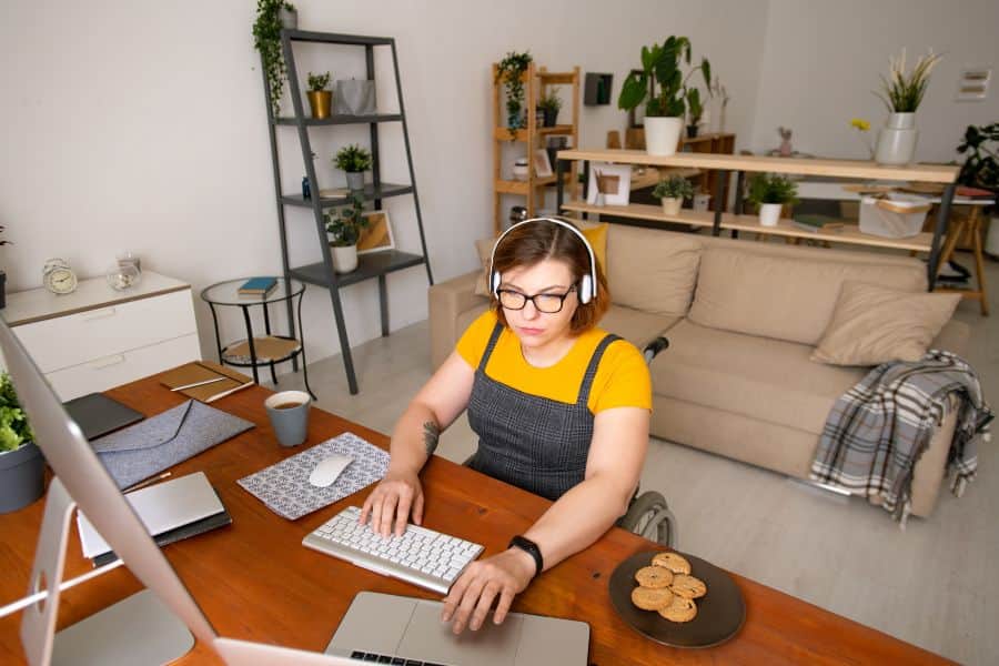 Person wearing headphones working at a home office desk with computer, coffee and cookies.