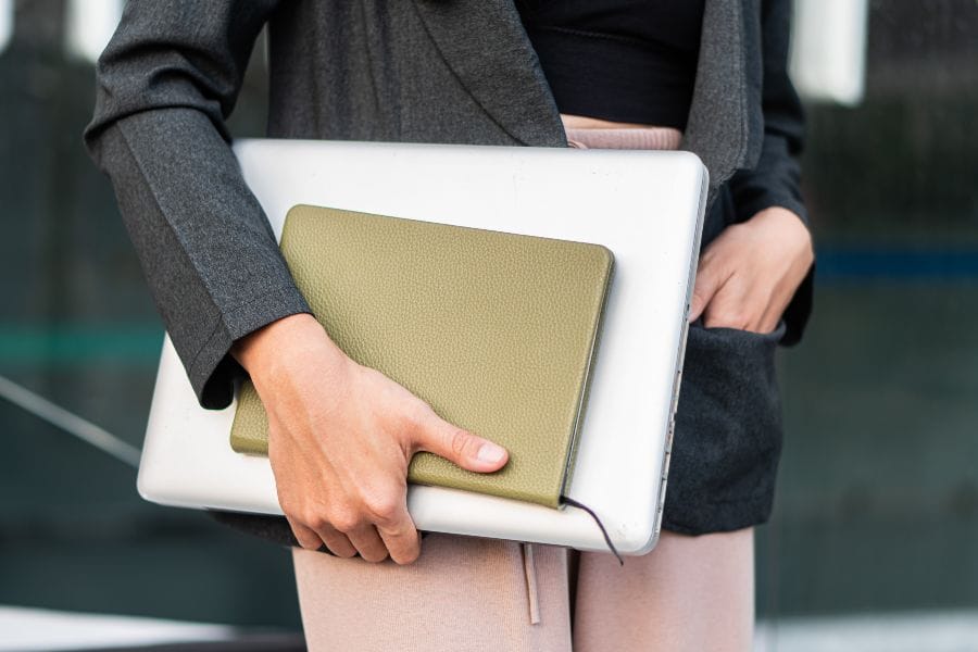 Person in business attire holding a laptop and notebook, ready to work between office and home.