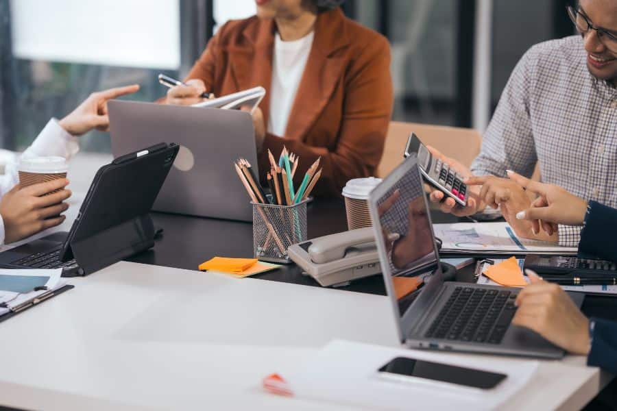 Team collaborating around laptops and tablets in an office meeting discussing hybrid work plans.