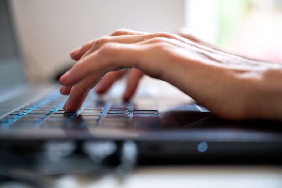 Close-up of hands typing on a laptop keyboard while working remotely.