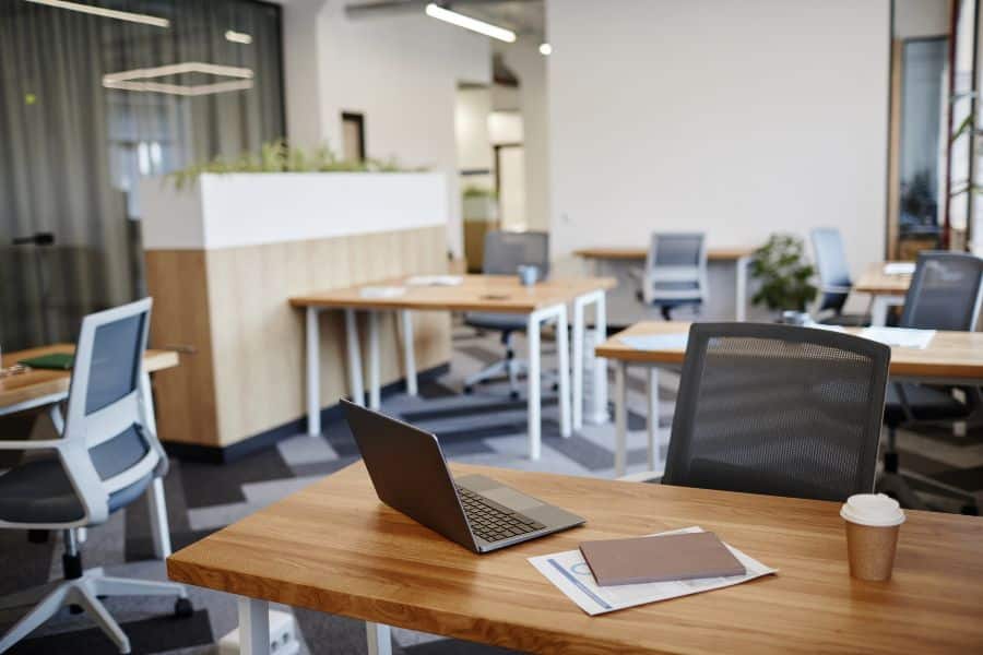 Empty modern coworking office with wooden desks, plants, and chairs for choosing ideal workspace.
