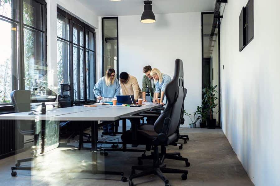 Diverse young professionals collaborate around glass table with laptops in sunny Sydney coworking space.