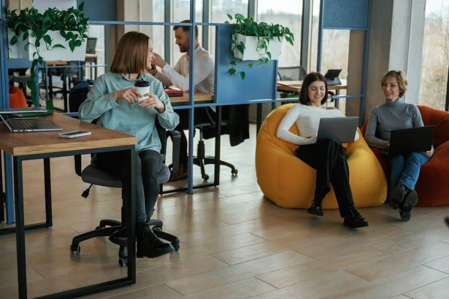 Women with coffee work on laptops near plants and yellow beanbag in cheerful Sydney coworking space.