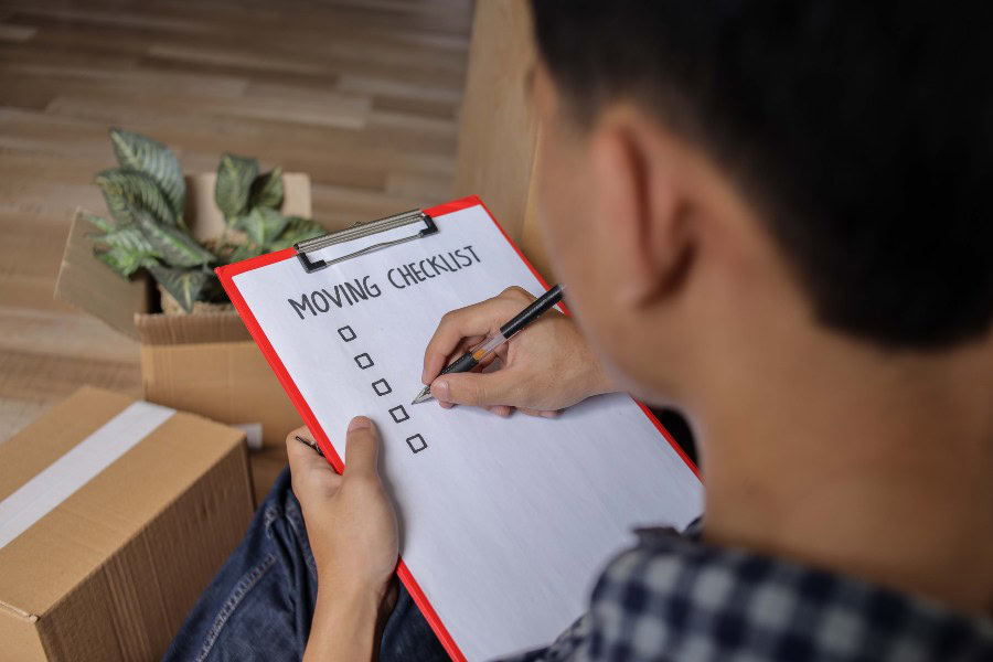 Person completing a moving checklist beside packed boxes in a new home.