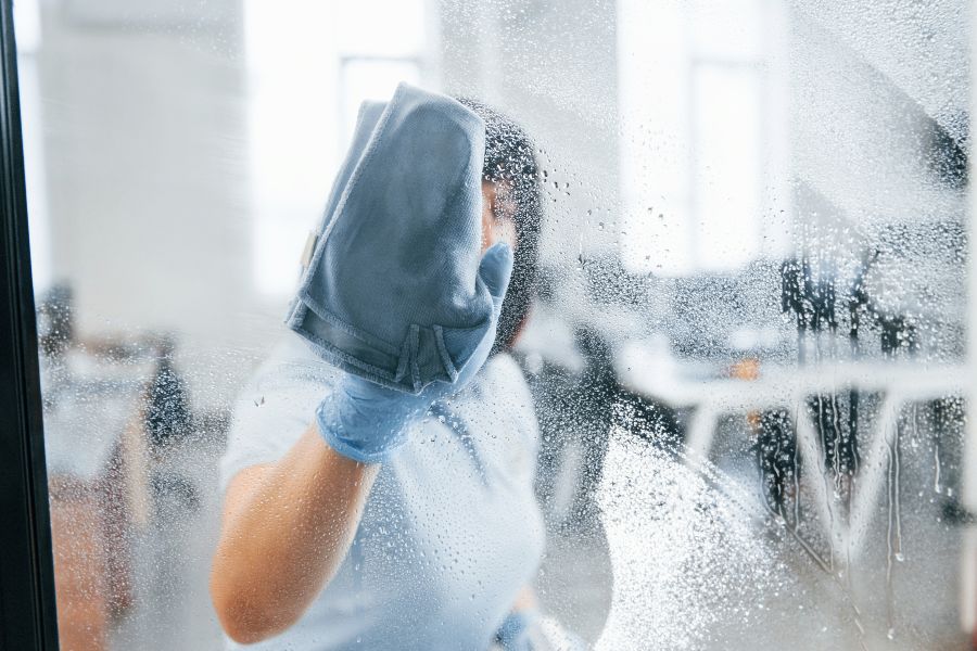 Person cleaning a dirty office window with a towel during move-out.